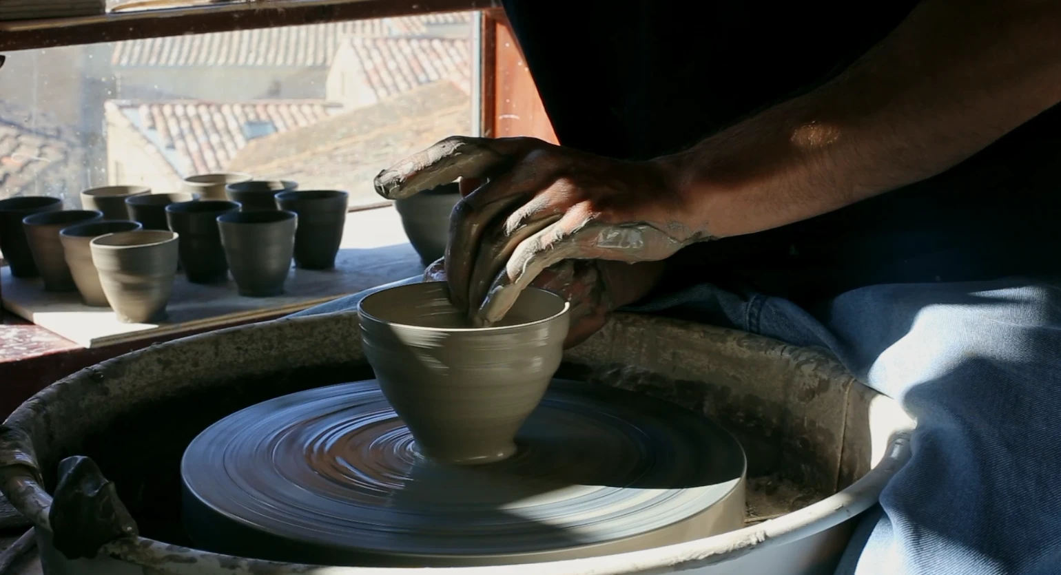 Tournage d'un bol devant la fenêtre de l'atelier, des gobelets crus sèchent sur le rebord